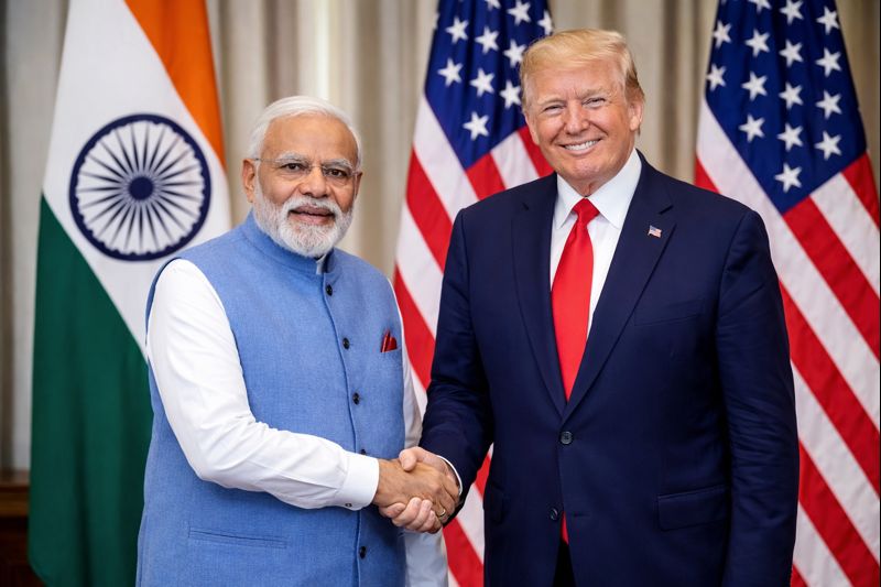 "Indian Prime Minister Narendra Modi shaking hands with former U.S. President Donald Trump in a formal meeting room, with Indian and American flags in the background, symbolizing India-US trade and economic cooperation talks."